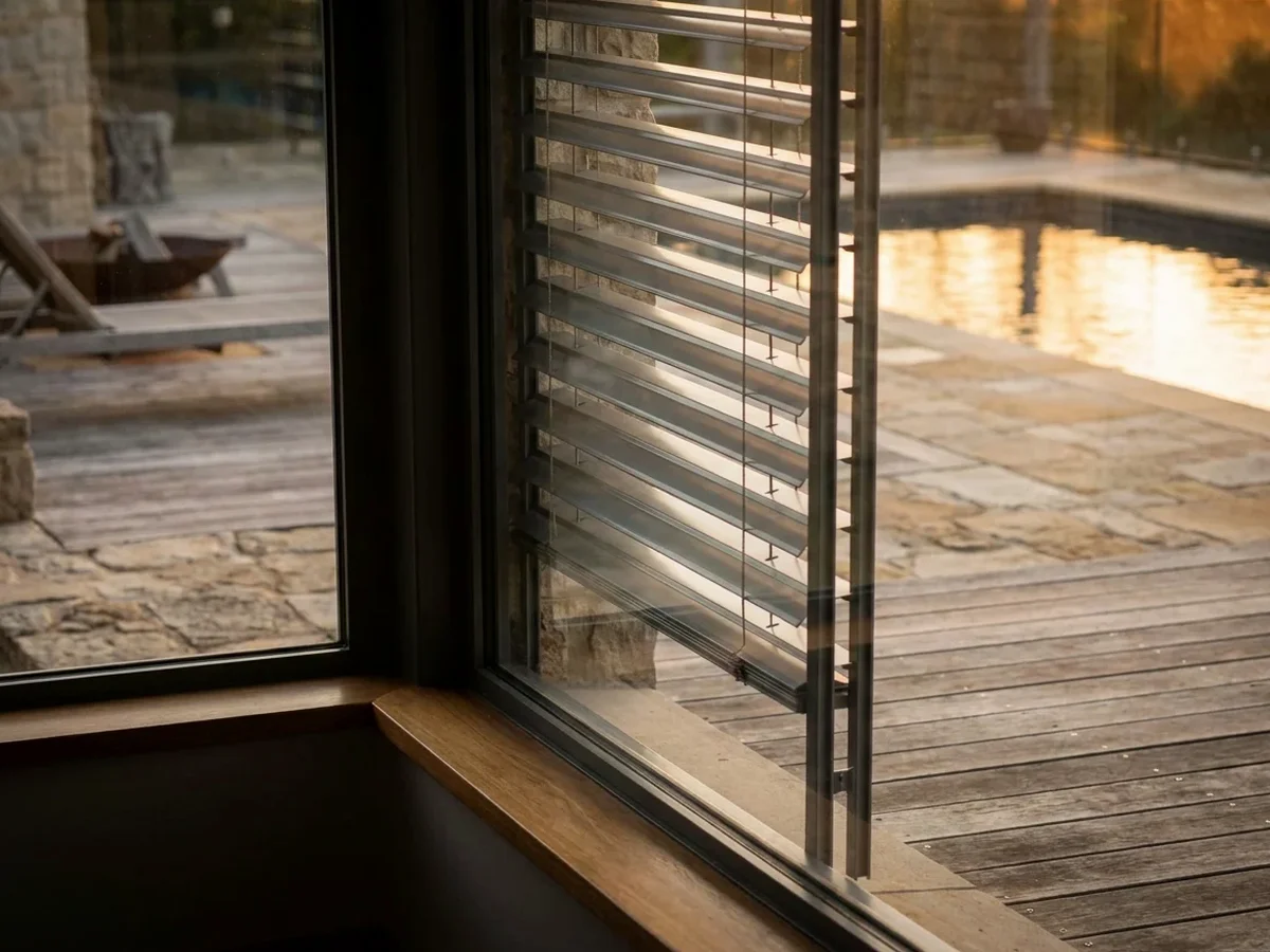 External venetian slats at dusk beside a pool deck, tilted to cut the low sun